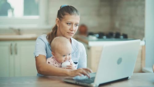 Mother Holds Baby While Working at Laptop