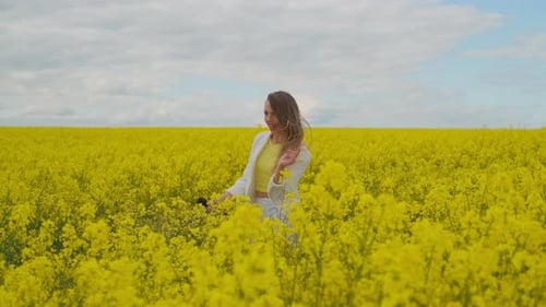 An Energetic Female Singer with a Microphone in a Field of Rapeseed with Yellow Flowers Jumps Shakes
