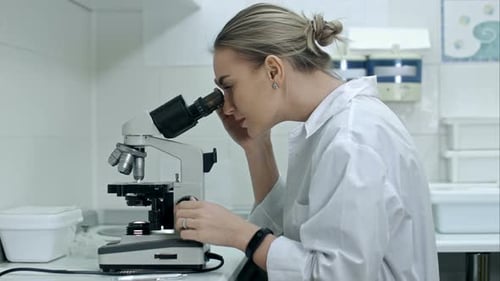 Young Scientist Analyzing Sample with Microscope in Lab