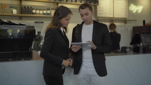 Concentrated Colleagues Surfing Internet on Tablet in Cafe with Blurred Bartender Preparing Order at