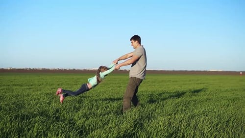 Junger Vater dreht seine Tochter im Kreis und hat Spaß in der Natur an einem hellen Tag
