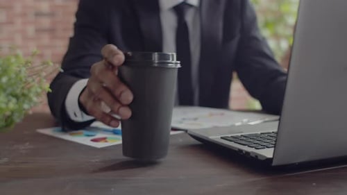 Paper glass of coffee is taken and drinks by a black man businessman from an office desk working
