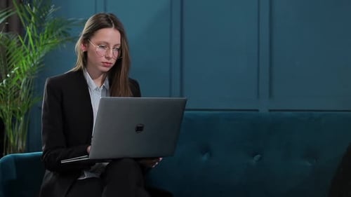 Portrait of an Elegant Businesswoman Sitting with Laptop on the Couch at the Luxury Blue Office