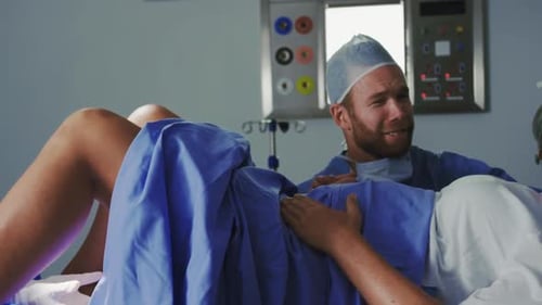 Side view of Caucasian female surgeon examining pregnant woman during labor in operation theater at