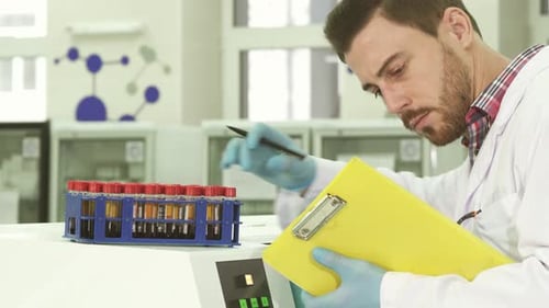 Ein junger Laborassistent nimmt Reagenzgläser mit Analysen heraus und schreibt Daten neu