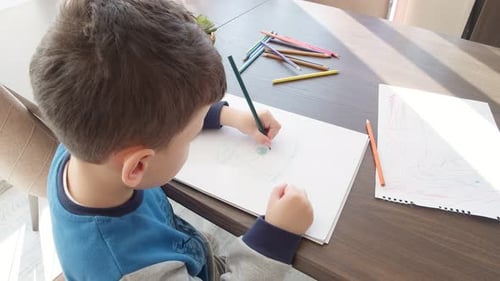 Child Drawing With Colored Pencil at Table Indoors