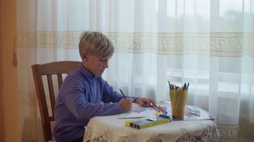Child Draws with Colored Pencils at Table