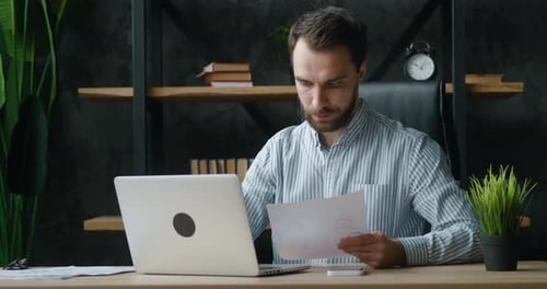 Focused Business Man Working with Paper Documents and Laptop at Modern Workplace