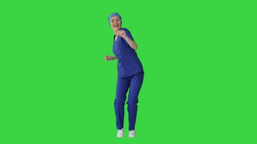 Smiling Female Medical Doctor in Blue Uniform Dancing and Cheering on a Green Screen, Chroma Key.