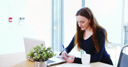 Woman Writes in Notebook While Using Smartphone