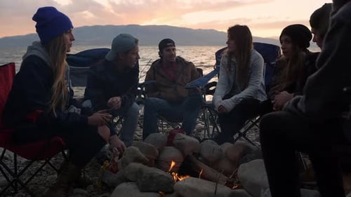 Group of family and friends gathered around campfire during sunset