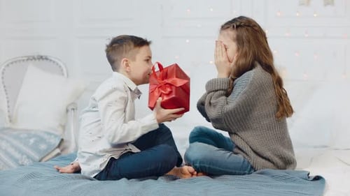 Boy Gives Gift to Smiling Girl on Bed
