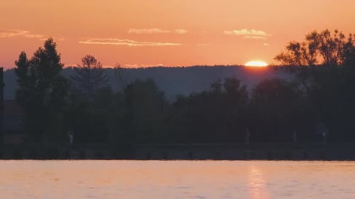 Seelandschaft mit dunkler Silhouette von Parkbäumen, die sich im Seewasser und in der Ferne spiegeln