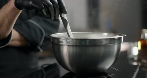 Der Küchenchef rührt langsam kochendes Essen in einer Metallschale bei schwacher Hitze in Zeitlupe um und schmilzt die Schokolade