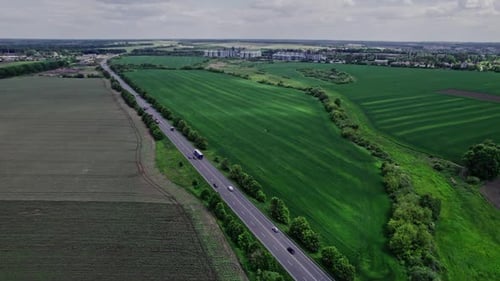 Cars Driving Along the Rustic Asphalt Road Between Fields