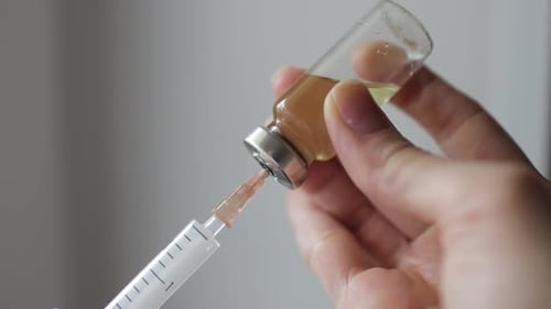 Frauenhände injizieren die Lösung mit einer Spritze in eine Durchstechflasche mit Impfstoff.