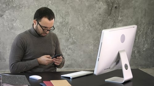 Man Typing on Phone at Computer Desk