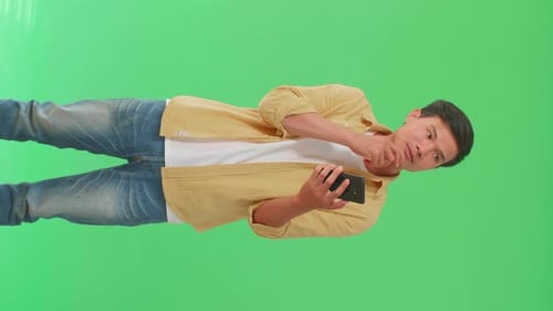 Asian Man Use Mobile Phone And Thinking About Something While Standing On Green Screen In The Studio