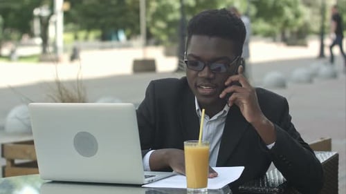 Young Afro American Businessman with Glasses and Laptop Sitting in Cafe Bar and Talking