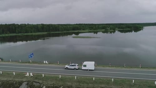 A Car with a Camper Trailer Rides Along a Dam Across a River in Canada. Drone
