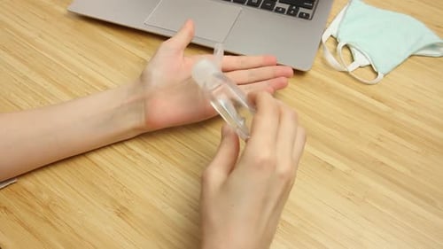Woman Applying Hand Sanitizer at Desk with Laptop