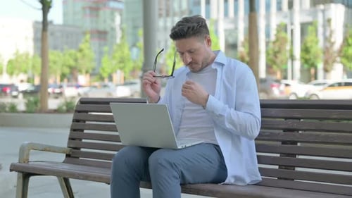 Man Using Laptop Experiences Eye Strain in Park
