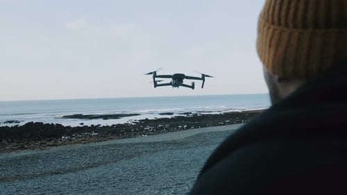 Un hombre con sombrero de cerca controla un Zumbido con control remoto, volando muy cerca en una hermosa y tranquila playa marina