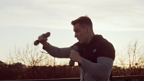 Man Training with Weights on Rooftop at Sunrise