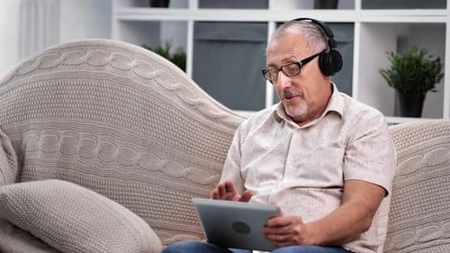Mature Man Chatting On Tablet With Headphones At Home