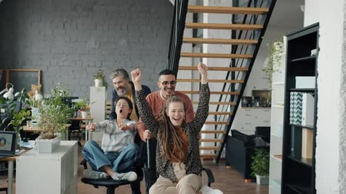 Slow Motion of Joyful Employees Having Fun in Office Riding Chairs Enjoying Work Break