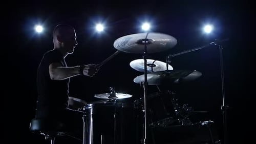 Musiker spielt professionell Musik am Schlagzeug. Schwarzer Hintergrund. Seitliche Ansicht. Hintergrundbeleuchtung. Silhouette