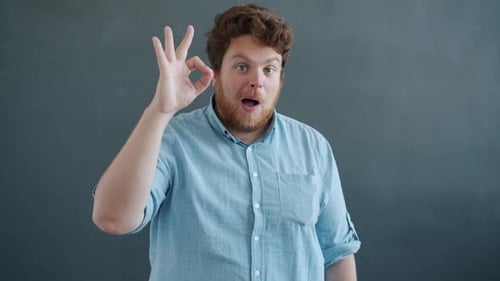 Man Gesturing Okay, Squinting Through Hand at Camera