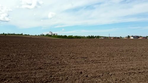 Vol d'observation aérienne par drone au-dessus d'un immense champ labouré et d'un ciel bleu