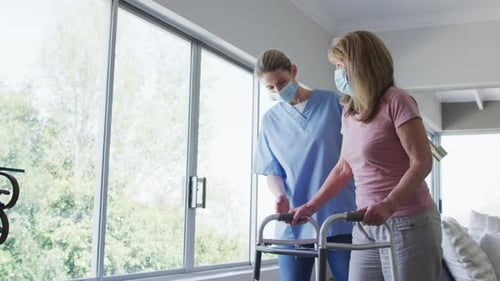 Female health worker assisting senior woman to walk with walking frame at home