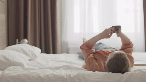 Young Woman Relaxes in Bed Using Phone