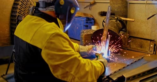 Schweißarbeiten im Werk. Mitarbeiter in Schutzmaske, Anzug und Handschuhen schweißt Metallteile mit