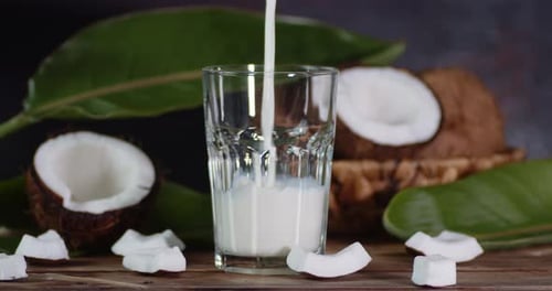 Coconut Milk Pouring Into a Glass. On a Dark Background.