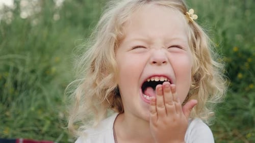 Niña rubia riendo de forma divertida cubriéndose la boca con la mano