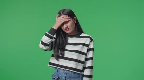 Asian Woman Having Headache While Standing In Front Of Green Screen Background
