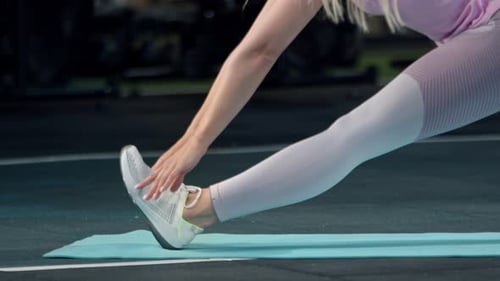 Flexible girl athlete does a back stretch on a karemat in the gym.