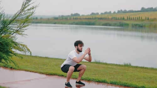 Man Doing Squats at Lakeside on Overcast Day
