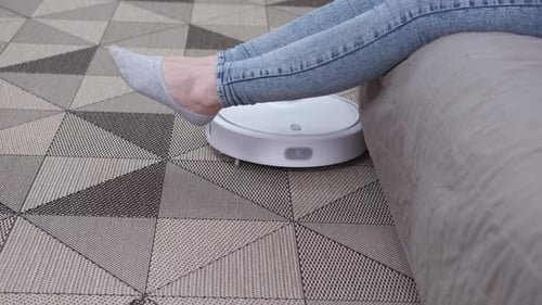 Robot Vacuum Cleans Carpet Near Resting Woman