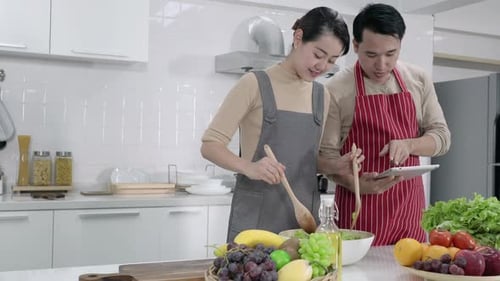 Couple Cooking Salad Together Using Tablet in Kitchen