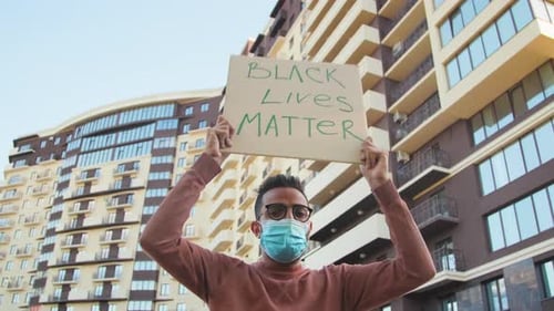 Masked Man Holds Protest Sign in City
