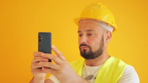 Man in Hard Hat Using Smartphone on Yellow Background