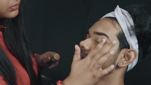 Professional make up artist contouring man's face in cosmetics studio