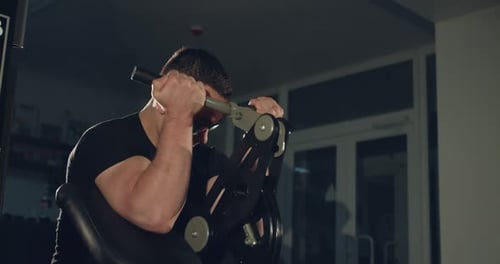 The Athlete with Glasses Works Out with the Simulator to Pump Arm Muscles in Gym