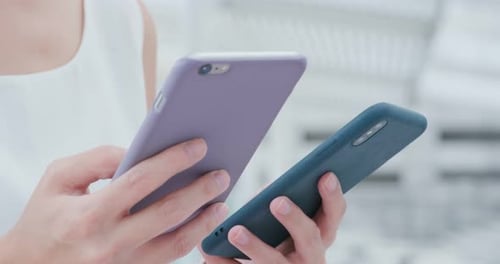 Person Holding Two Mobile Phones in Urban Setting