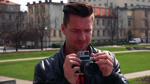 A Young Handsome Man Takes Photos with a Camera - Face Closeup - a Building and a Park