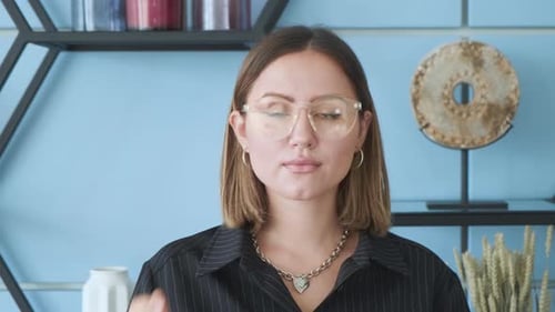 Woman Adjusts Glasses in Front of Blue Wall